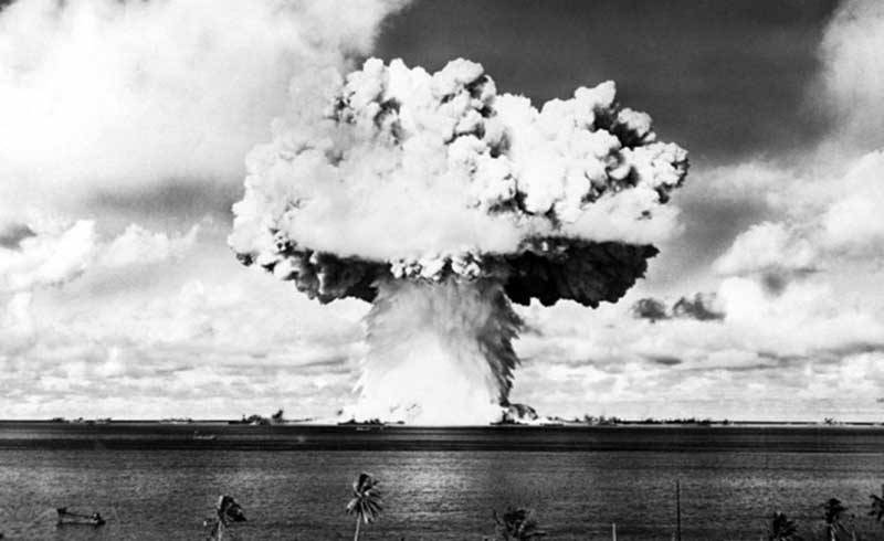 Historic photograph of an atomic bomb test showing a massive mushroom cloud rising above the ocean. This powerful image symbolizes the destructive force of nuclear weapons and the dawn of the atomic age.