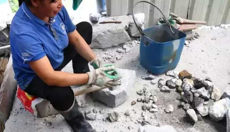 A woman uses a geology hammer to break rocks, keeping high-quality tungsten ore for further crushing and processing.