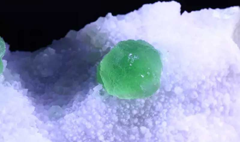 green fluorite sphere resting on a bed of fine white crystals