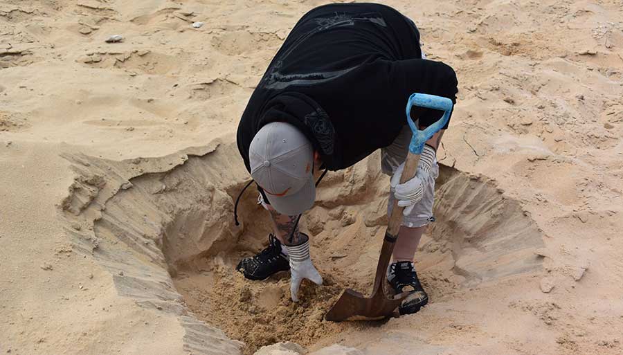 A person excavating in sandy terrain, searching for desert rose crystals formed from gypsum in arid environments.