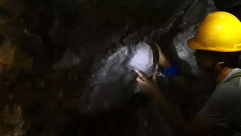 Miner extracting tungsten ore from a rock face inside a dark underground mine