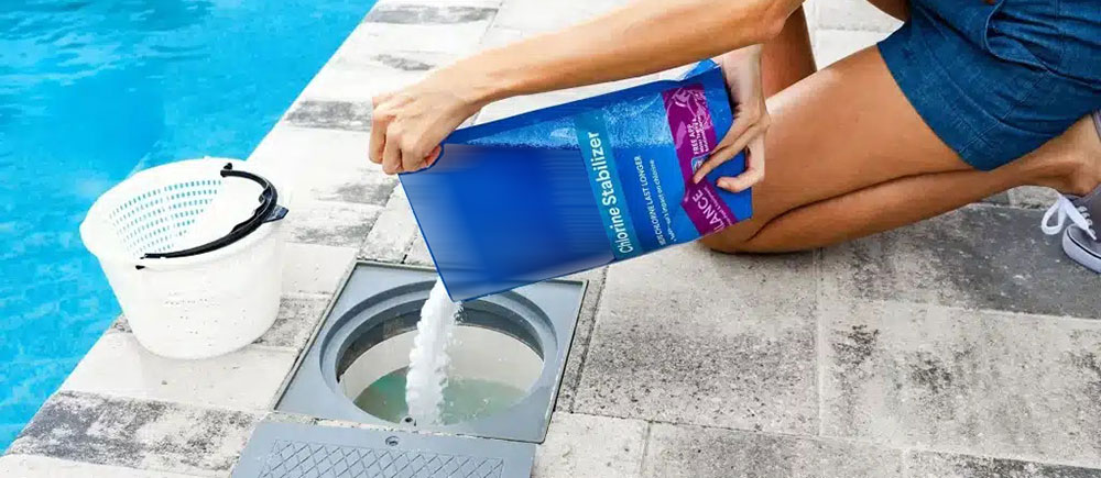 Person pouring cyanuric acid chlorine stabilizer granules into a swimming pool system for water treatment and disinfection